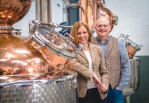 Paul and Tiffany Kerruish, co-founders of Fynoderee Distillery stand next to a still in a warehouse.