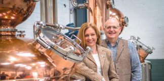 Paul and Tiffany Kerruish, co-founders of Fynoderee Distillery stand next to a still in a warehouse.