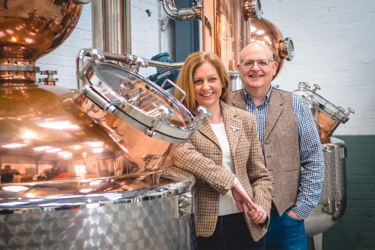 Paul and Tiffany Kerruish, co-founders of Fynoderee Distillery stand next to a still in a warehouse.