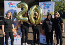 The SGF Healthy Living Programme team stand holding a two balloon and a zero balloon together in front of HLP branded stands.