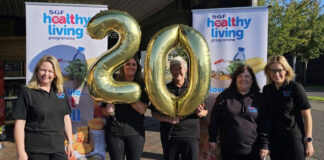 The SGF Healthy Living Programme team stand holding a two balloon and a zero balloon together in front of HLP branded stands.