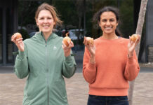 Two people stand holding onions in front of a building.