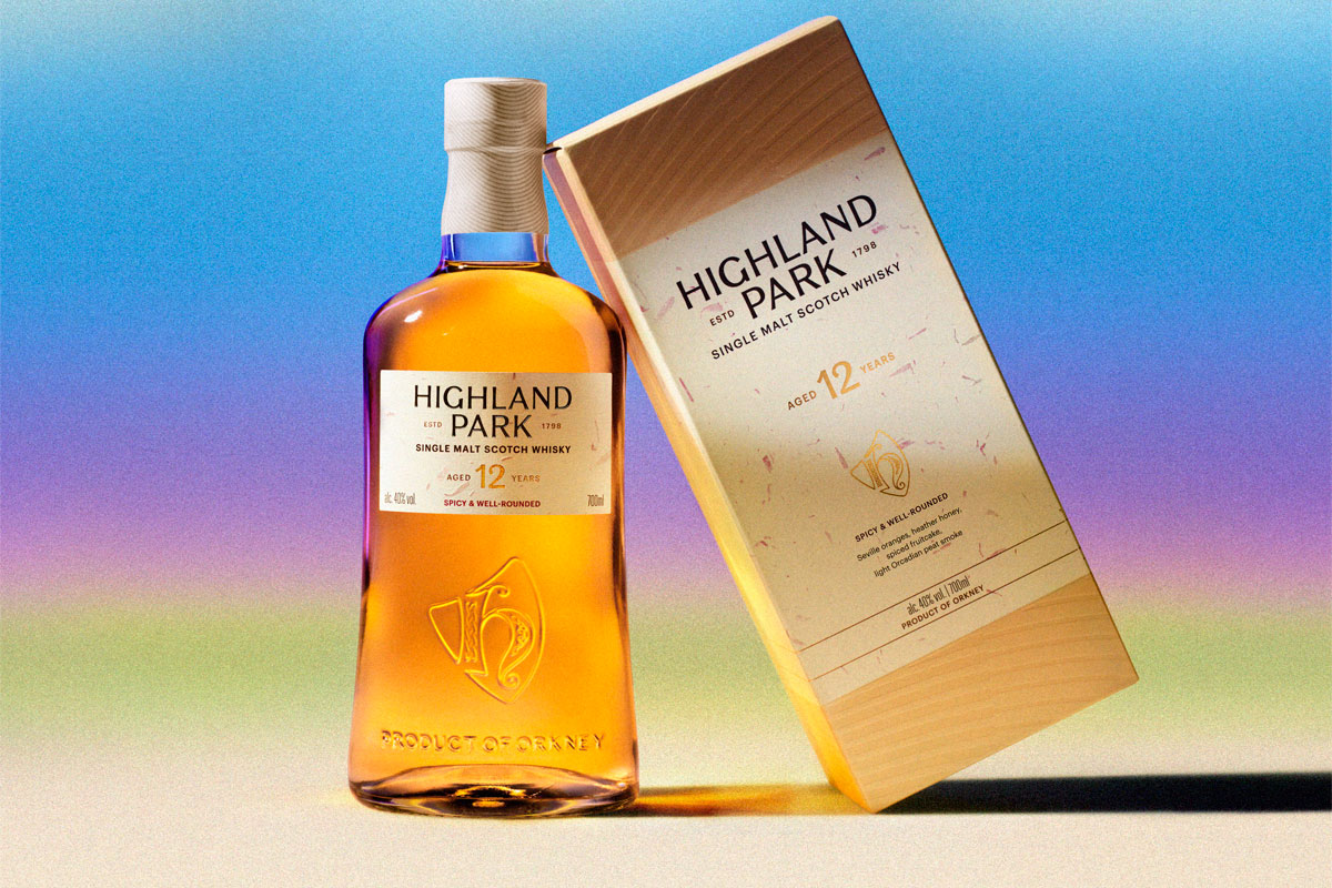 A bottle of the new look for Highland Park stands next to the new packaging design for the box with a colour gradient background.