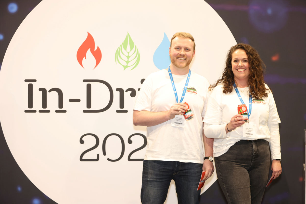 L-R Joe Harris, Lonkero and Paige Gibbons, Lonkero both stand in front of the In-Drinks logo holding cans of Lonkero.