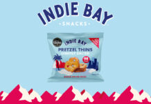 A pack of Indie Bay Snacks Pretzel Thins Lightly Salted is against a blue background with a red mountain range under it and the Indie Bay logo above the pack.