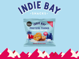 Kestrel Foods acquires Indie Bay Snacks A pack of Indie Bay Snacks Pretzel Thins Lightly Salted is against a blue background with a red mountain range under it and the Indie Bay logo above the pack.