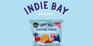 A pack of Indie Bay Snacks Pretzel Thins Lightly Salted is against a blue background with a red mountain range under it and the Indie Bay logo above the pack.