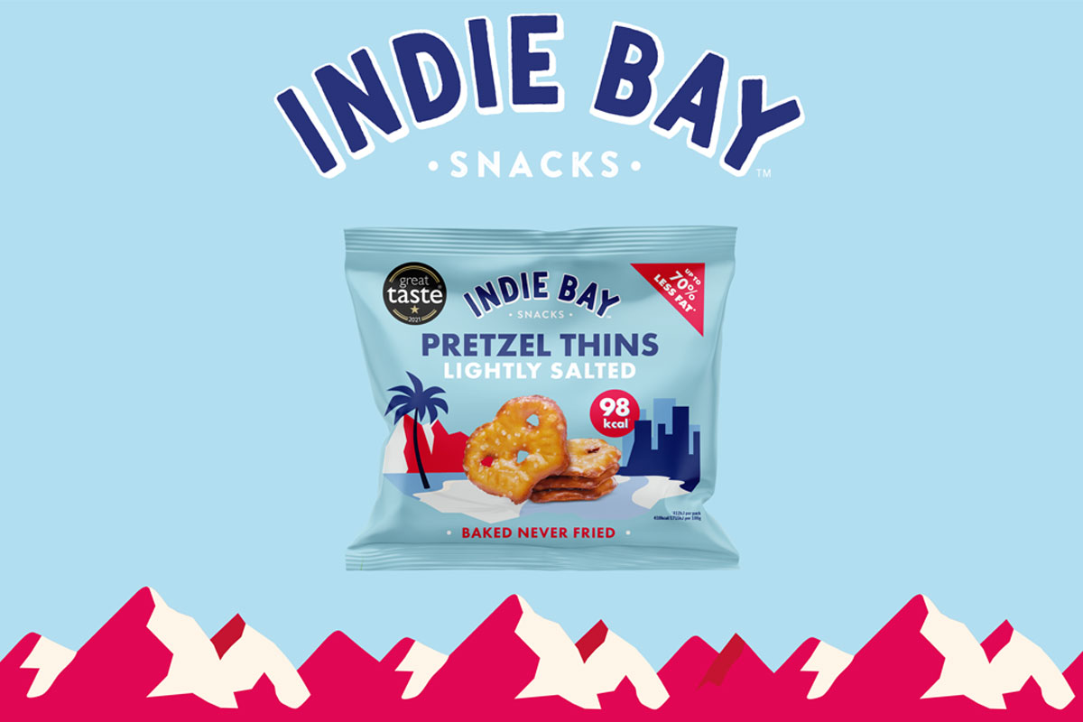 A pack of Indie Bay Snacks Pretzel Thins Lightly Salted is against a blue background with a red mountain range under it and the Indie Bay logo above the pack.