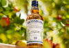 A bottle of Mossburn Speyside Single Malt 12 YO Domaine Dupont Calvados Cask Finish stands in an apple orchard.