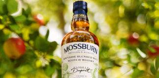 A bottle of Mossburn Speyside Single Malt 12 YO Domaine Dupont Calvados Cask Finish stands in an apple orchard.