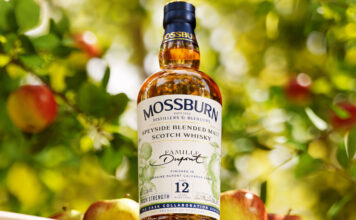 A bottle of Mossburn Speyside Single Malt 12 YO Domaine Dupont Calvados Cask Finish stands in an apple orchard.