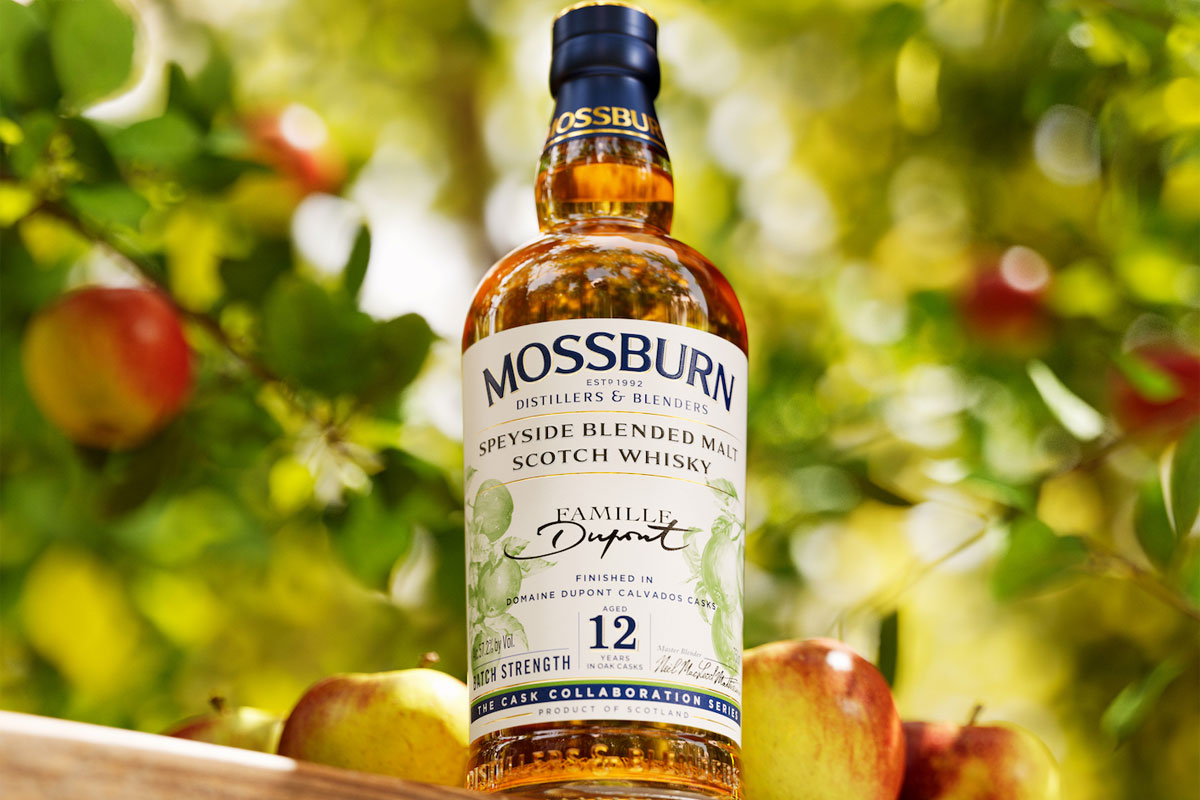 A bottle of Mossburn Speyside Single Malt 12 YO Domaine Dupont Calvados Cask Finish stands in an apple orchard.