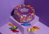 Promotional image of Quality Street paper tubs featuring the tub and sweets from the tub against a purple background.