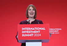 Chancellor of the exchequer Rachel Reeves stands at a podium with the text "International Investment Summit 2024" against a red backdrop.