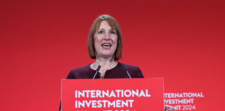 Chancellor of the exchequer Rachel Reeves stands at a podium with the text "International Investment Summit 2024" against a red backdrop.