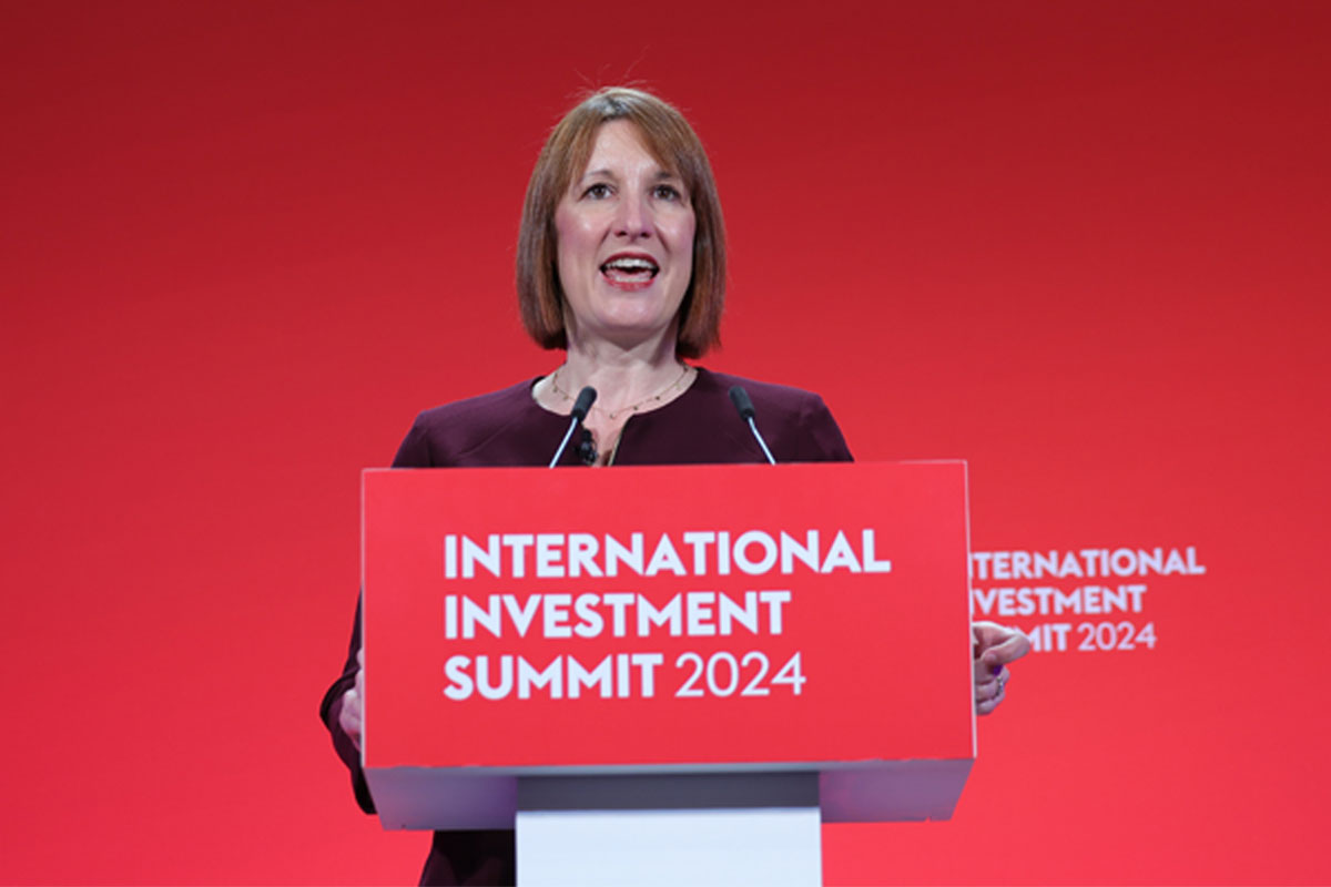 Chancellor of the exchequer Rachel Reeves stands at a podium with the text "International Investment Summit 2024" against a red backdrop.