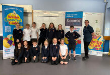 A group of kids in school sit between banners for the Healthy Living Programme Welby Breakfast Club and Scotmid Co-op.