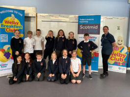 Scotmid pledges support to the HLP A group of kids in school sit between banners for the Healthy Living Programme Welby Breakfast Club and Scotmid Co-op.