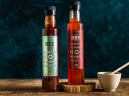 Scottish Bee Company jumps on hot honey trend Bottles of The Scottish Bee Company Hot Honey stand on a wooden table including Kimchi Hot Honey Drizzle and Scotch Bonnet Hot Honey Drizzle with a small ceramic bowl with a honey dipper stick in it.