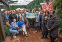 A group of retailers stand together for the *Shopt Refer a Friend Scheme launch with a neon sign of the *shopt logo.