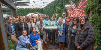 A group of retailers stand together for the *Shopt Refer a Friend Scheme launch with a neon sign of the *shopt logo.