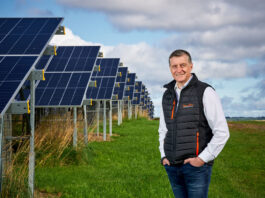 Simon Howie powers on renewables Simon Howie, owner of Simon Howie Group, stands in front of rows of solar panels.