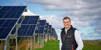 Simon Howie, owner of Simon Howie Group, stands in front of rows of solar panels.