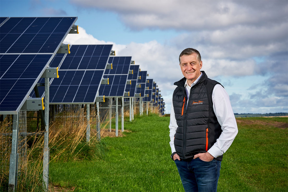 Simon Howie, owner of Simon Howie Group, stands in front of rows of solar panels.