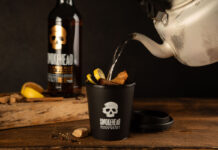 Someone pours boiling water from a kettle into a Smokehead branded cup to make a Hot Toddy cocktail with a bottle of Smokehead whisky behind it.