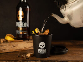 Someone pours boiling water from a kettle into a Smokehead branded cup to make a Hot Toddy cocktail with a bottle of Smokehead whisky behind it.