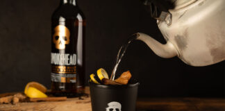 Someone pours boiling water from a kettle into a Smokehead branded cup to make a Hot Toddy cocktail with a bottle of Smokehead whisky behind it.