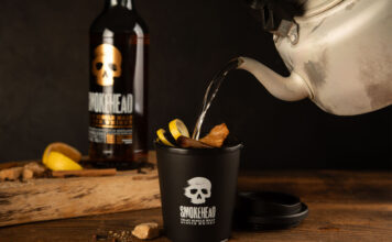 Someone pours boiling water from a kettle into a Smokehead branded cup to make a Hot Toddy cocktail with a bottle of Smokehead whisky behind it.