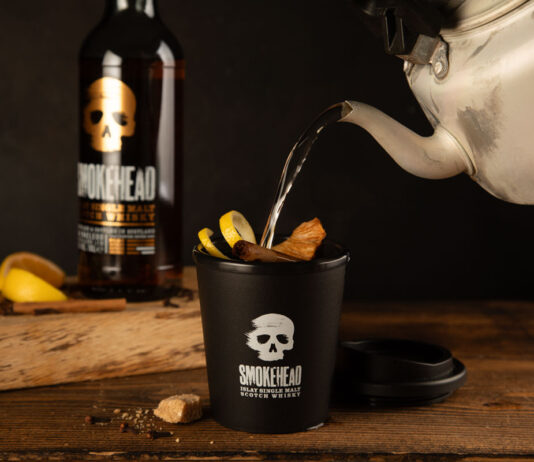Clear the head with a Smokehead Hot Toddy Someone pours boiling water from a kettle into a Smokehead branded cup to make a Hot Toddy cocktail with a bottle of Smokehead whisky behind it.