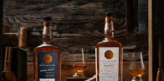 Bottles of Stanhope Kentucky Whiskey Bourbon and Rye Whiskey stands on a wooden table with nosing glasses containing the whiskies.