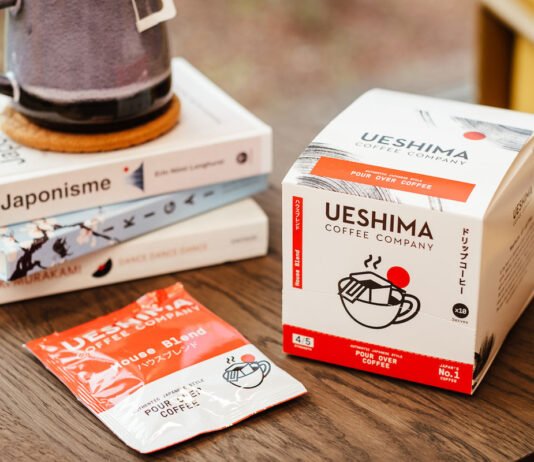 Ueshima Pours Over new Coffee Bags Ueshima Coffee Company Pour Over Coffee Bags box with a sachet of the coffee bag next to it with a pile of books on a wooden table.