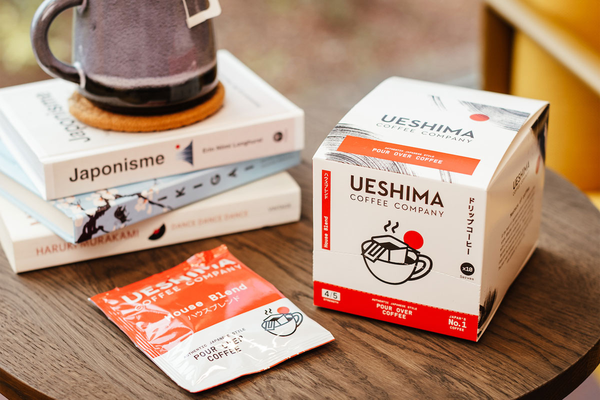 Ueshima Coffee Company Pour Over Coffee Bags box with a sachet of the coffee bag next to it with a pile of books on a wooden table.