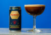 A can of Whitebox Cocktails' Collina & Co Espresso Martini serve stands next to a coupe glass with the cocktail inside, both stand on a tabletop against a blue background.