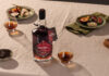 A bottle with Eden Mill Pedro Ximénez Single Cask sits on a table with food on plates and a nosing glass with a sample of the whisky inside.