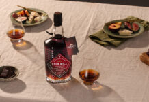 A bottle with Eden Mill Pedro Ximénez Single Cask sits on a table with food on plates and a nosing glass with a sample of the whisky inside.