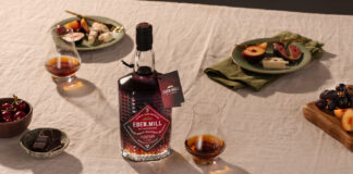 A bottle with Eden Mill Pedro Ximénez Single Cask sits on a table with food on plates and a nosing glass with a sample of the whisky inside.