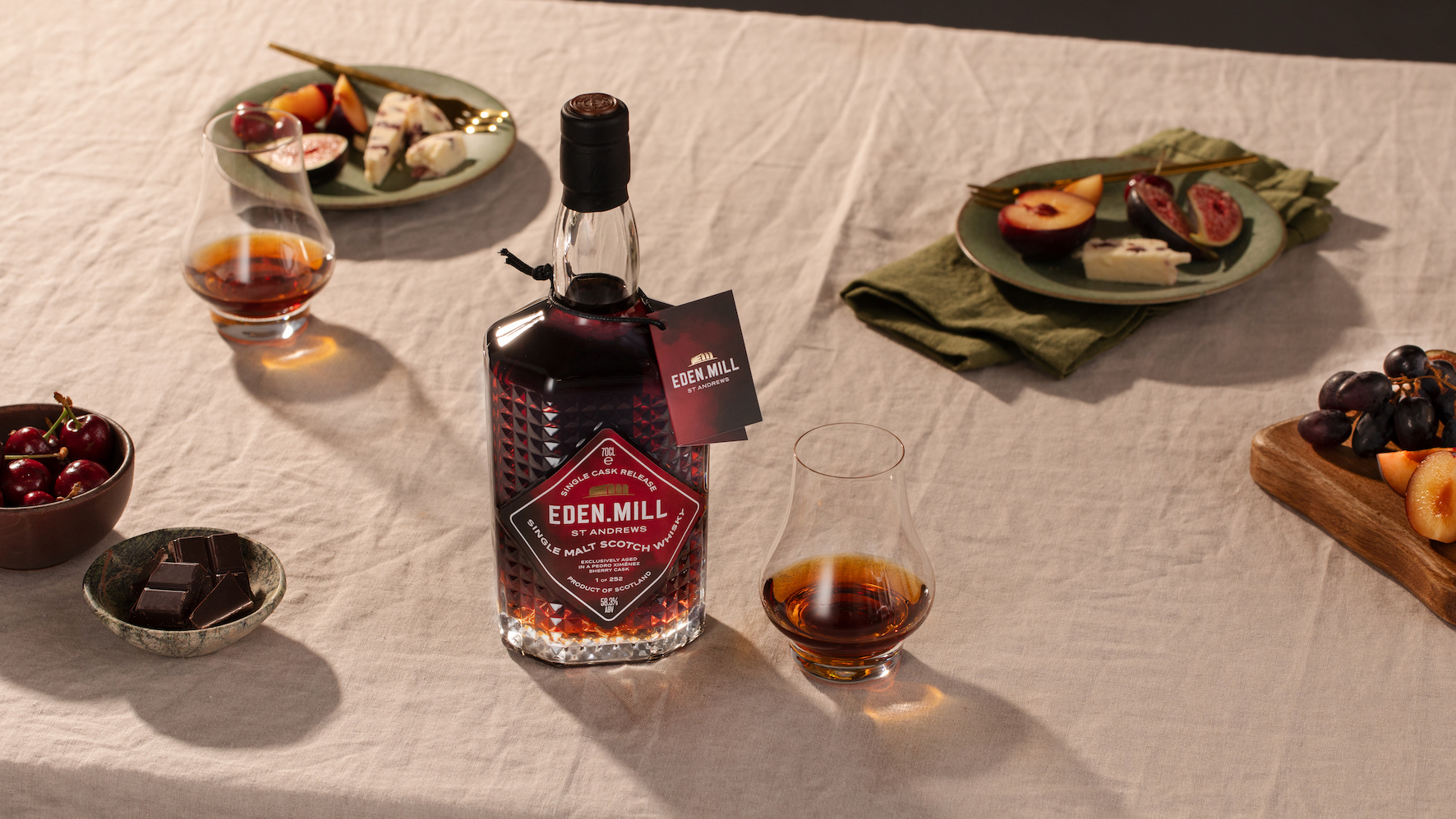 A bottle with Eden Mill Pedro Ximénez Single Cask sits on a table with food on plates and a nosing glass with a sample of the whisky inside.