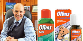 Dr Roger Henderson, GP and spokesperson for Olbas, sits at a table with pack shots of Olbas Bath and Olbas For Children Inhalant Decongestant Oil.