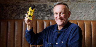 Paul Crawford, founder of Panther M*lk sits in a booth with cartons of Panther Shake whilst holding one.