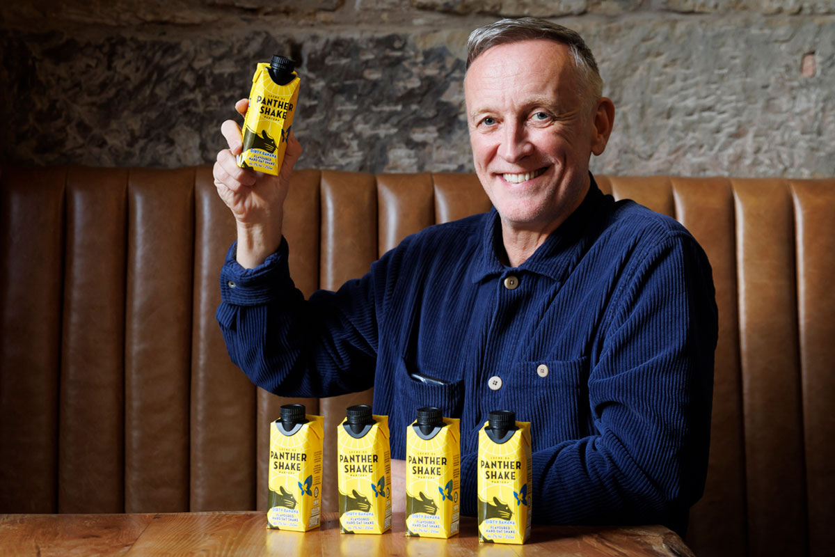 Paul Crawford, founder of Panther M*lk sits in a booth with cartons of Panther Shake whilst holding one.