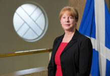 Shona Robison, cabinet secretary for finance and local government, stands in Scottish Parliament in front of the Scotland flag.