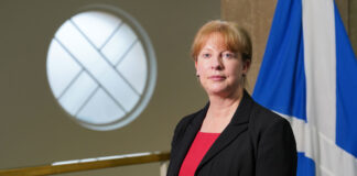 Shona Robison, cabinet secretary for finance and local government, stands in Scottish Parliament in front of the Scotland flag.