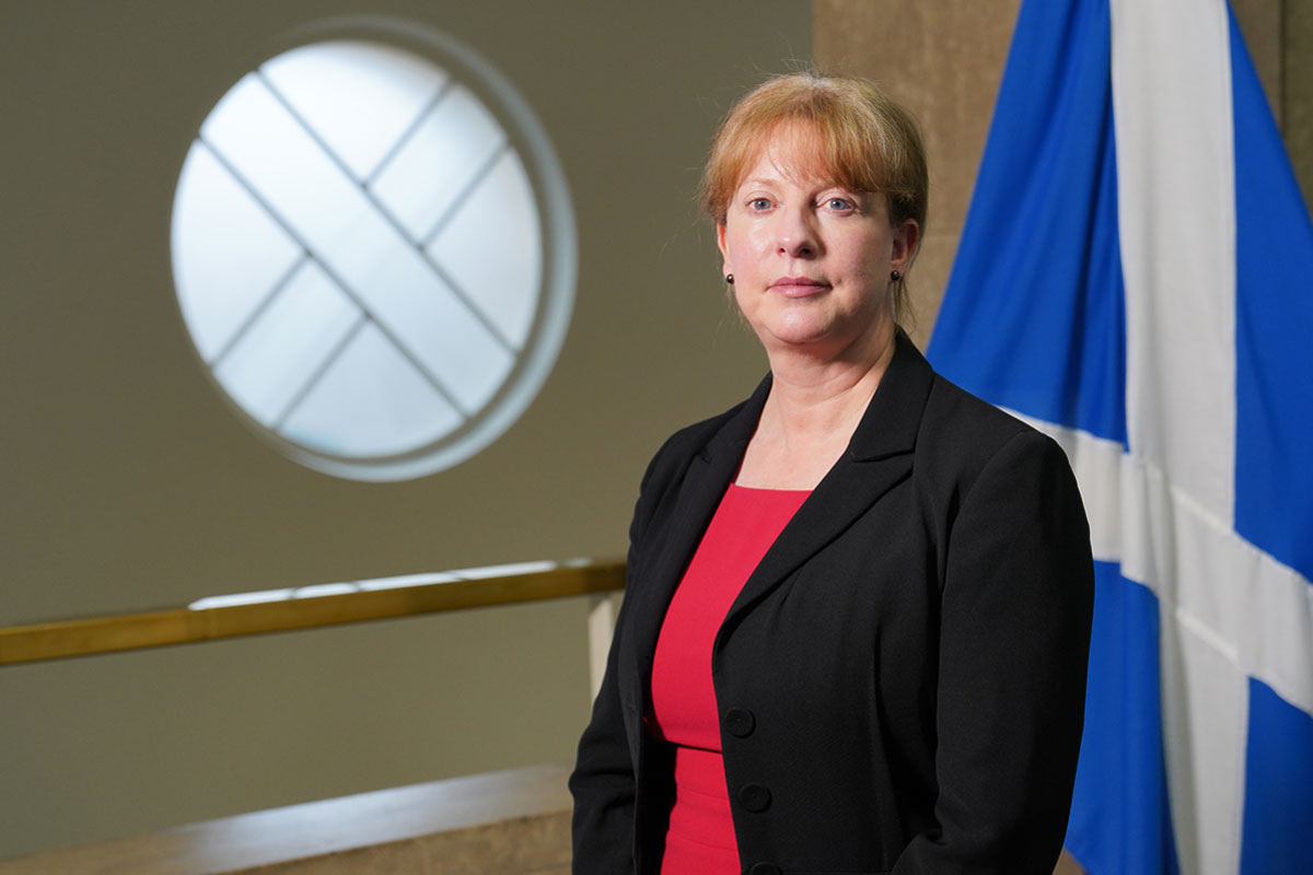 Shona Robison, cabinet secretary for finance and local government, stands in Scottish Parliament in front of the Scotland flag.