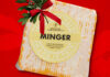 A packet of Aldi Minger Cheese is set against a red background with a sprig of Mistletoe on top of it.