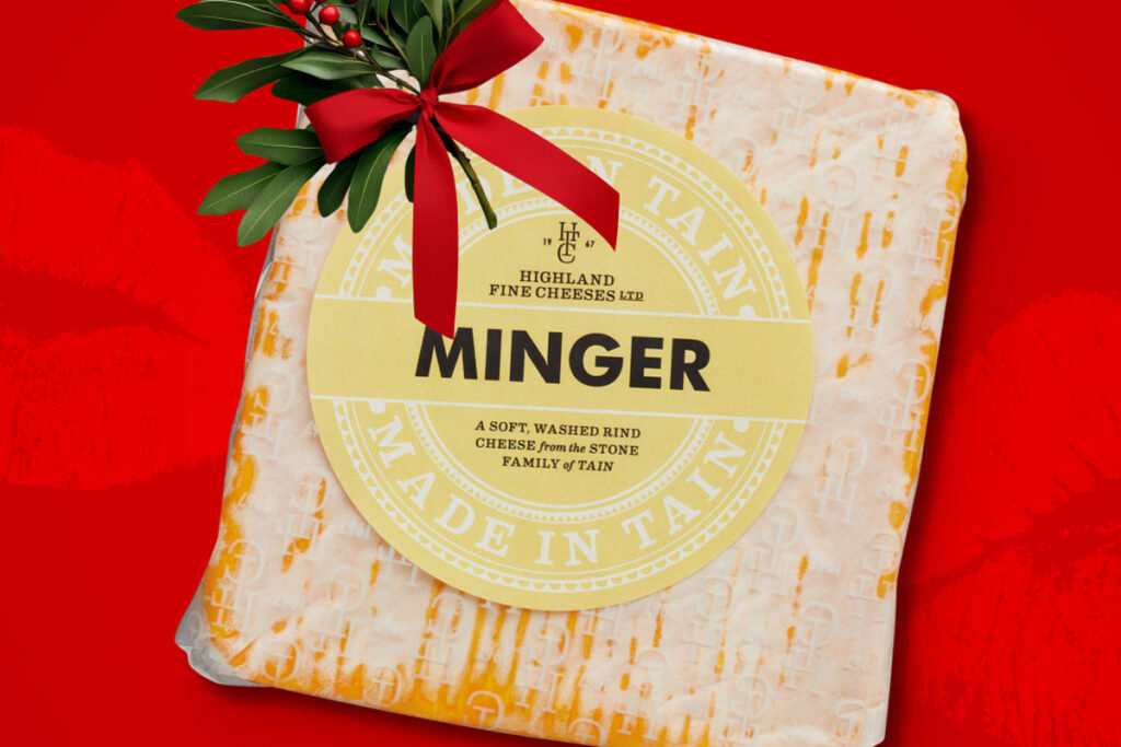 A packet of Aldi Minger Cheese is set against a red background with a sprig of Mistletoe on top of it.