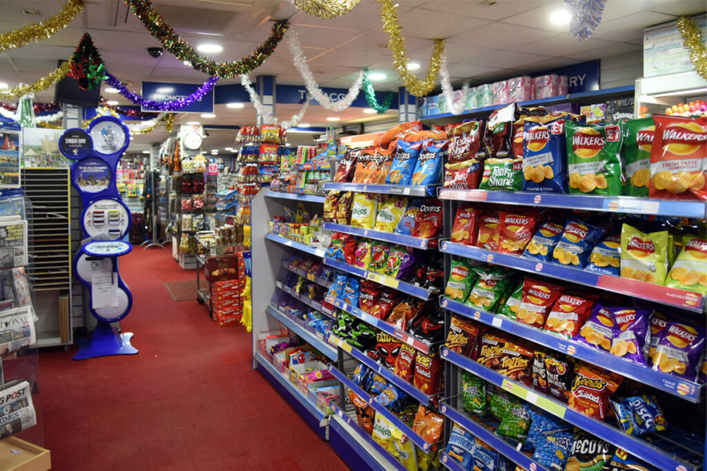 A shop floor with crisps on the shelves to the right and tinsel hanging from the roof.